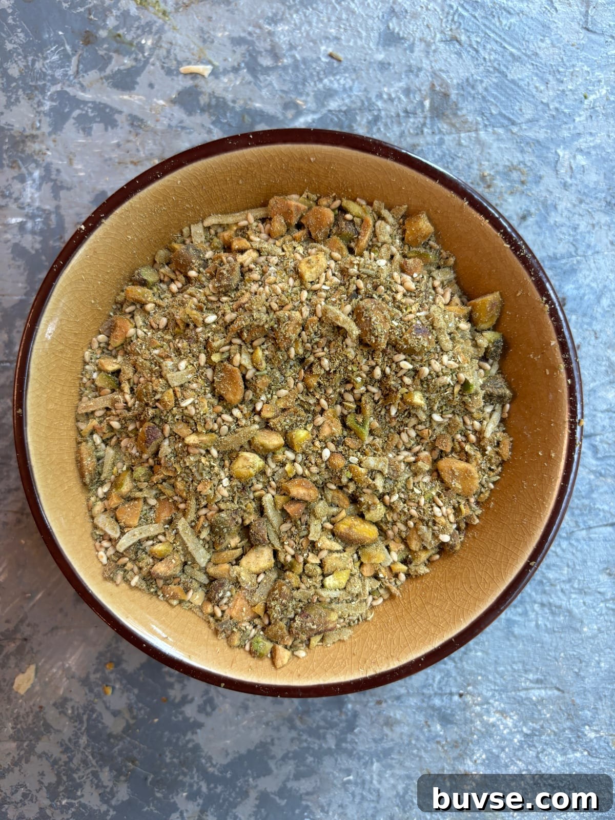 overhead image of ground fennel, cumin, and coriander seeds mixed in a small bowl with pistachios and sesame seeds