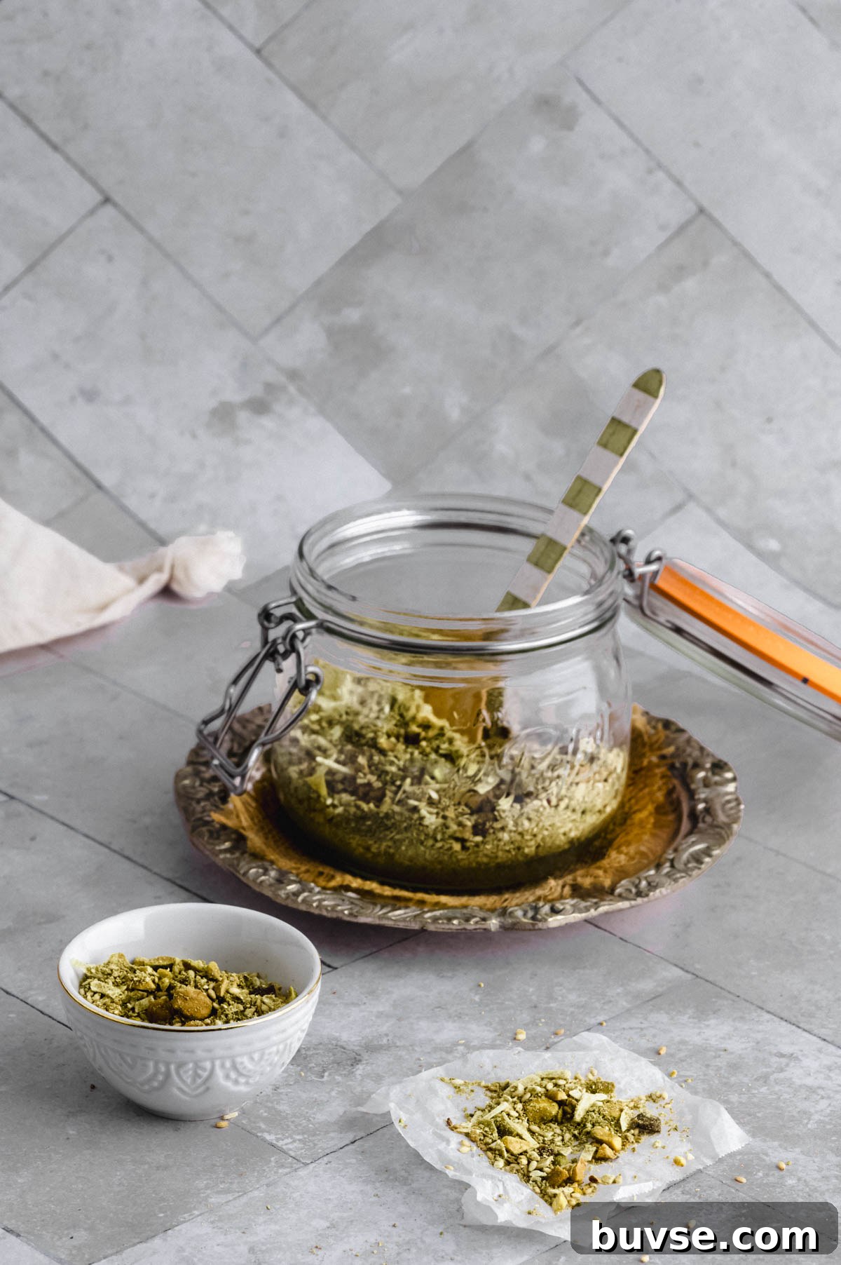 A small bowl with Dukkah next to a container filled half way with pistachio copconut dukkah