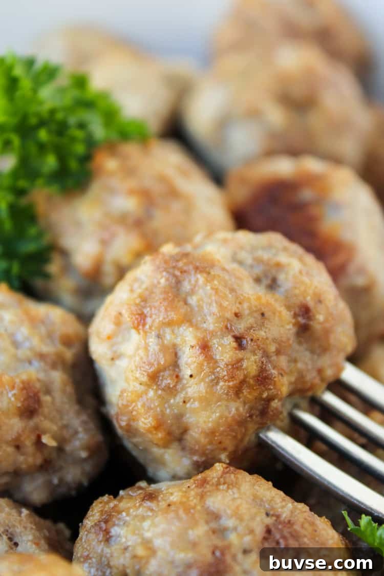 a fork spearing a baked meatball with parsley garnish.
