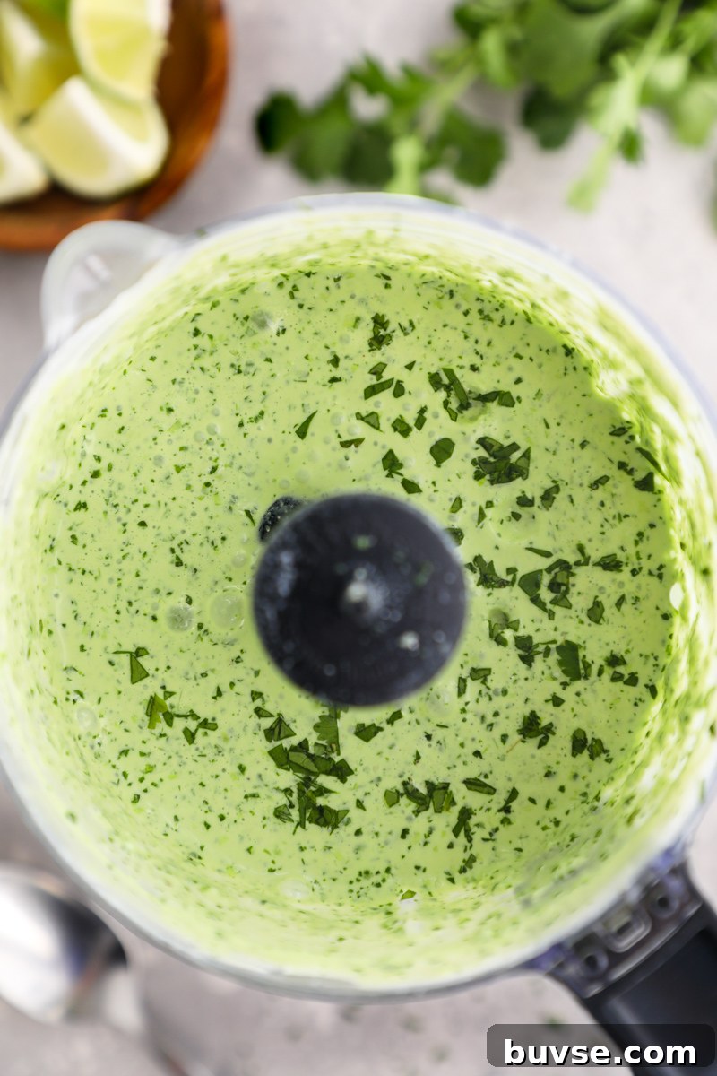 Authentic Peruvian Aji Verde Green Sauce Recipe 4 A food processor photographed from above filled with creamy spicy Peruvian green sauce surrounded by a bowl of lime wedges and fresh cilantro