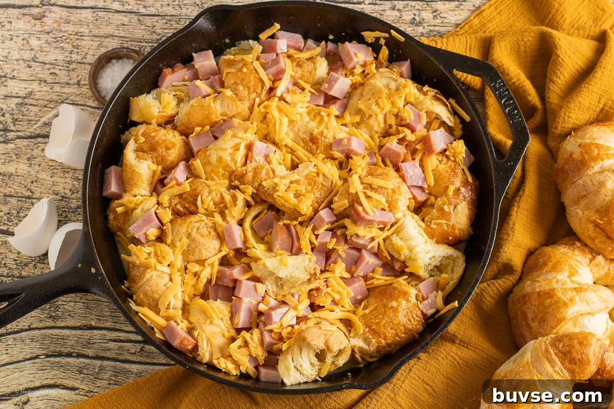 uncooked ham and cheese croissant casserole in a cast iron skillet