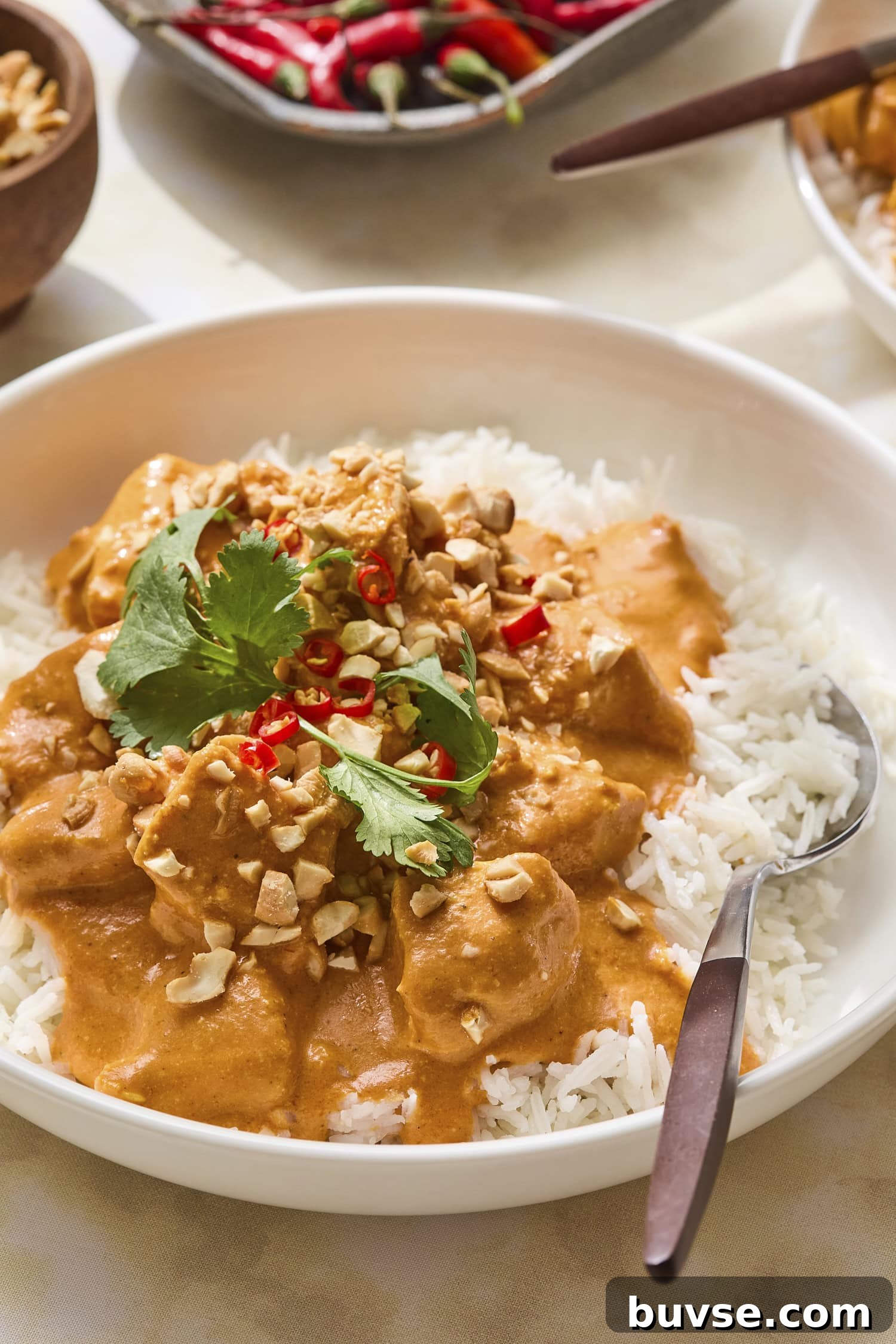 White rice with orange colored butter chicken with cashews and cilantro on top.