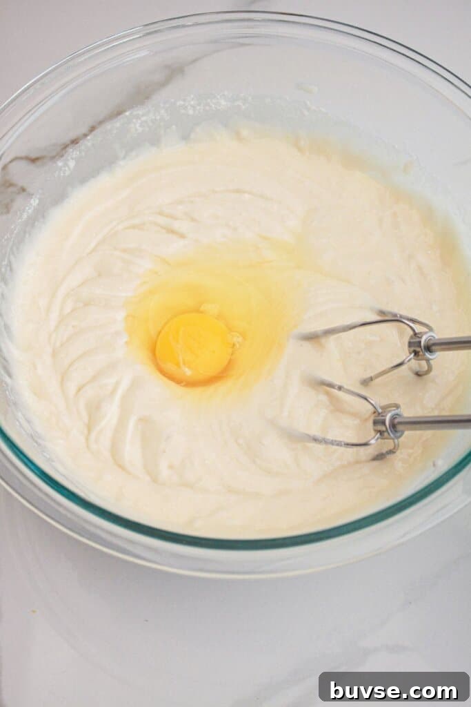 Vanilla Sheet Cake Recipe with Strawberry Frosting 5 Egg being added to cake batter.